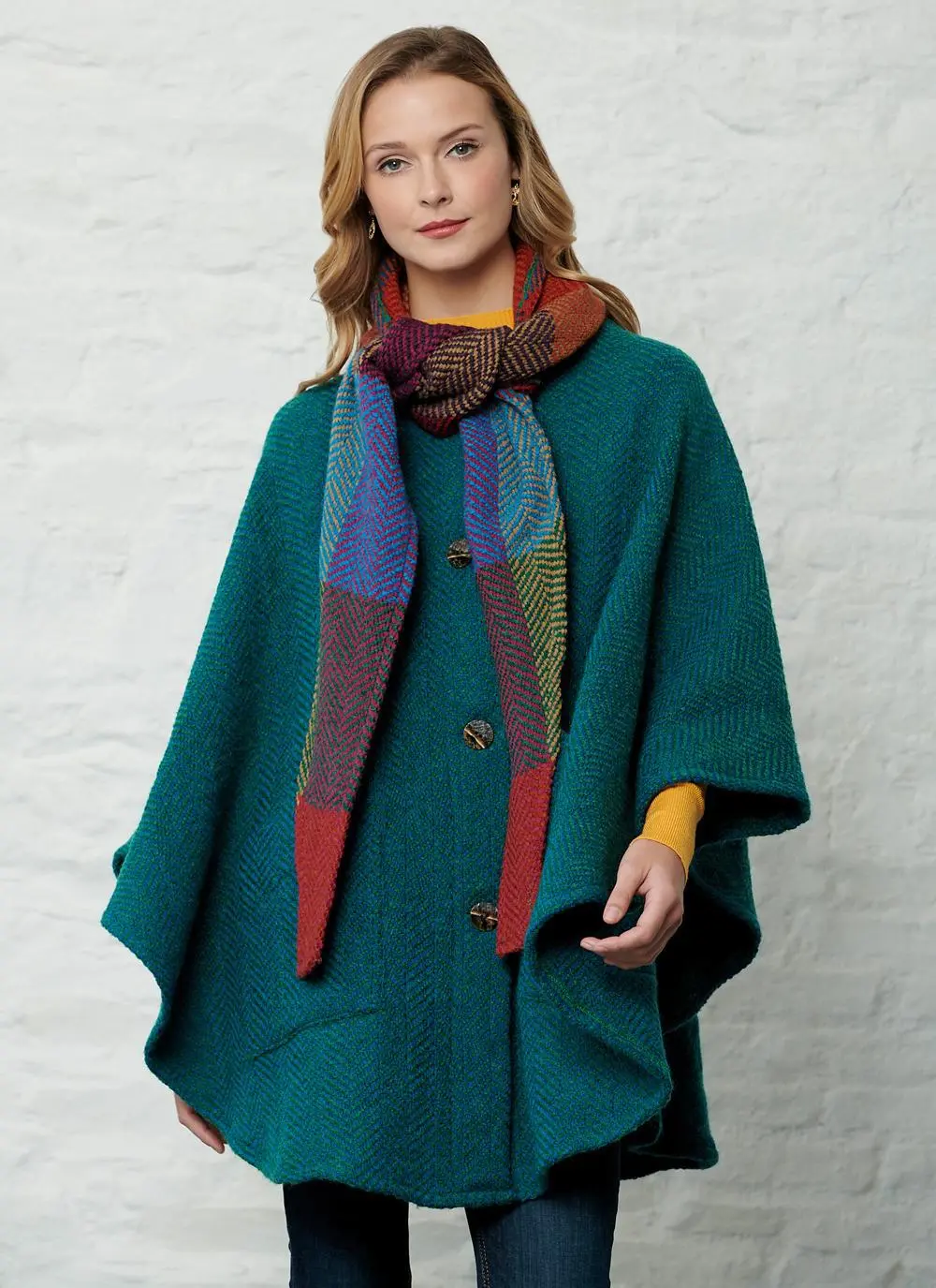 Studio shot of women wearing green cape with detachable multi-colored hood with hands by side.
