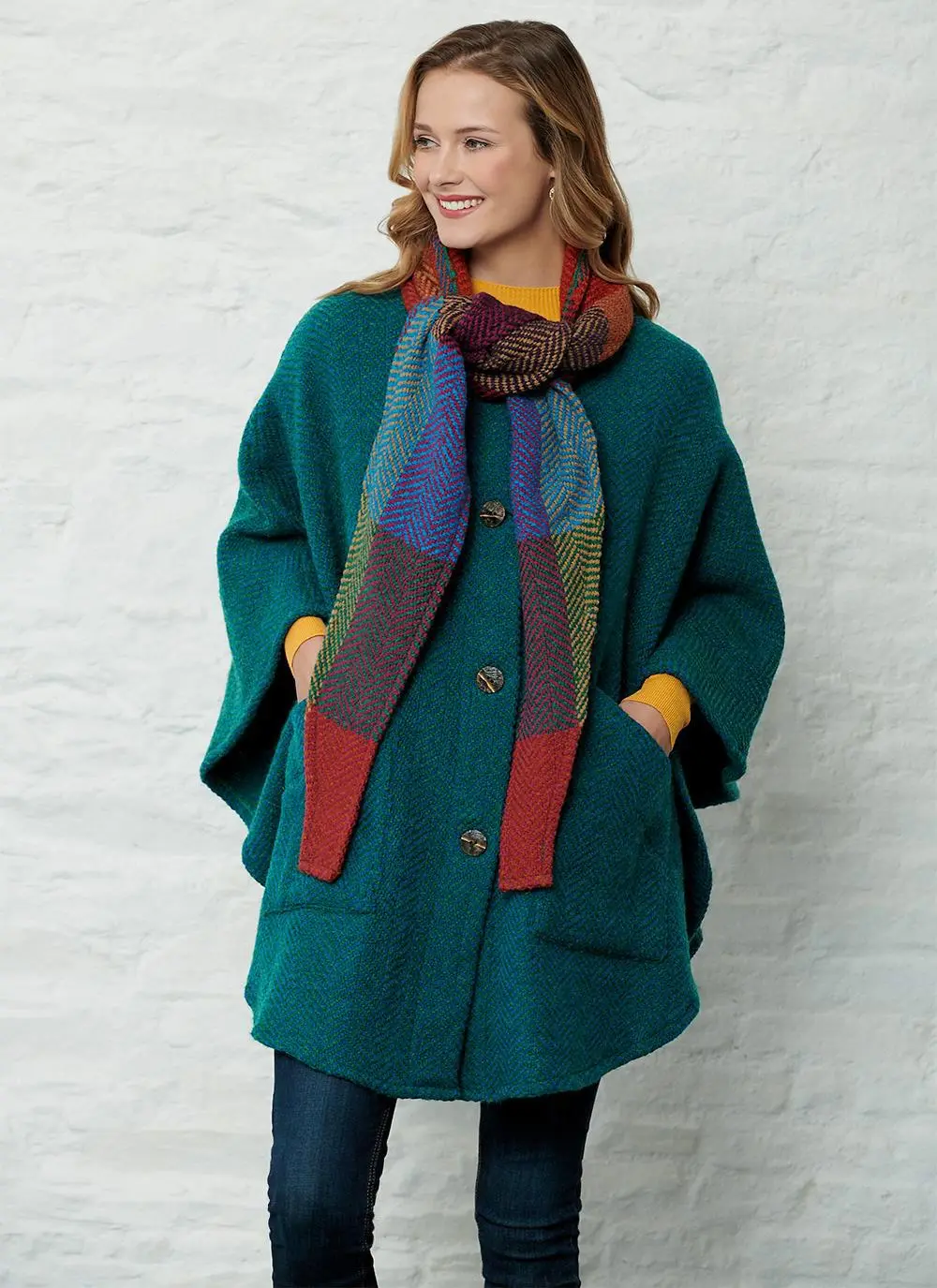 Studio shot of women wearing green cape with detachable multi-colored hood with both hands in pockets.