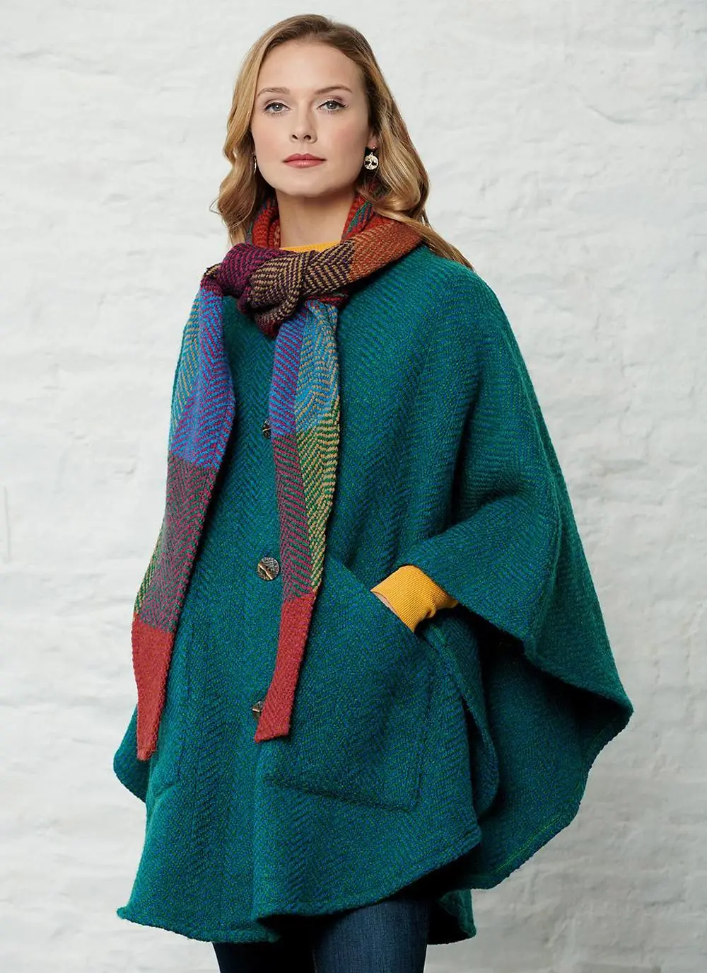 Studio shot of women wearing green cape with detachable multi-colored hood with hand in pocket.