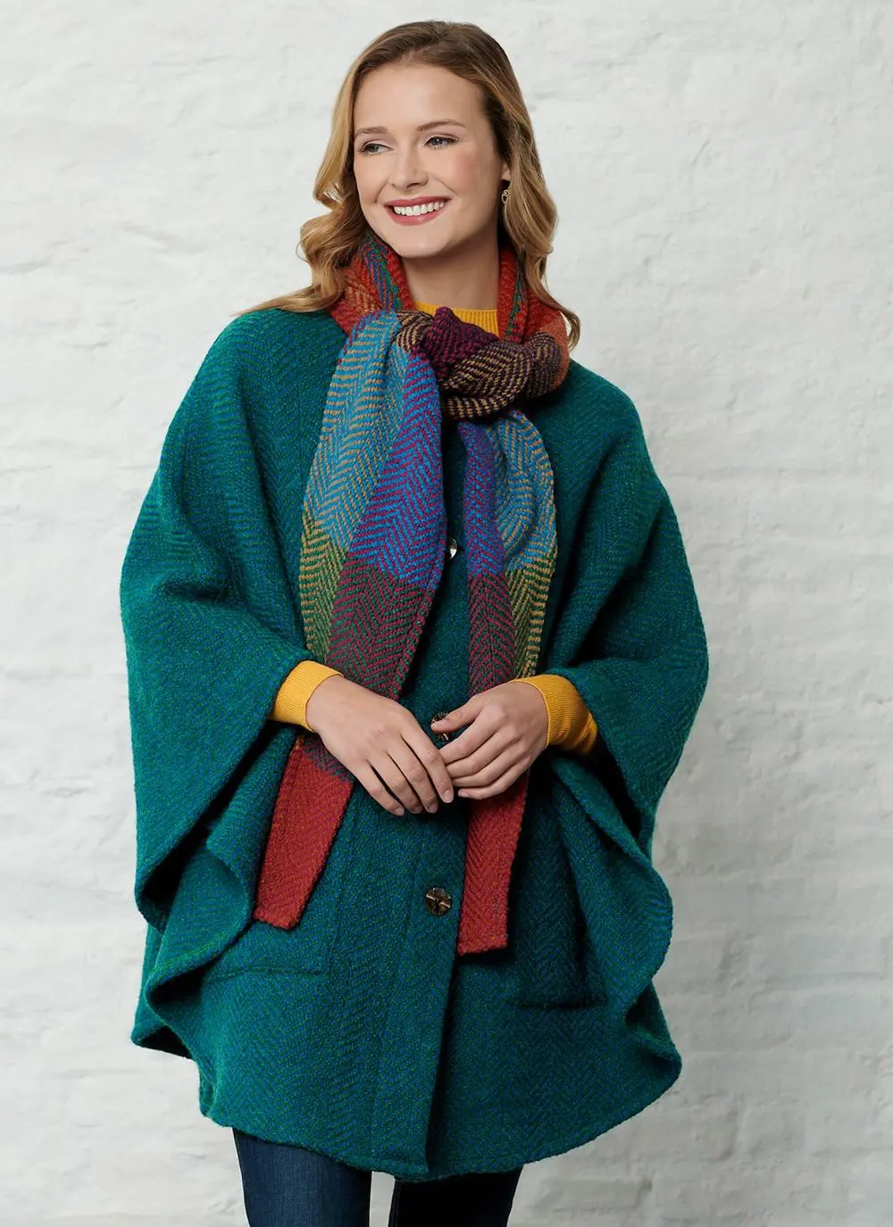 Studio shot of women wearing green cape with detachable multi-colored hood with hands clasped. 