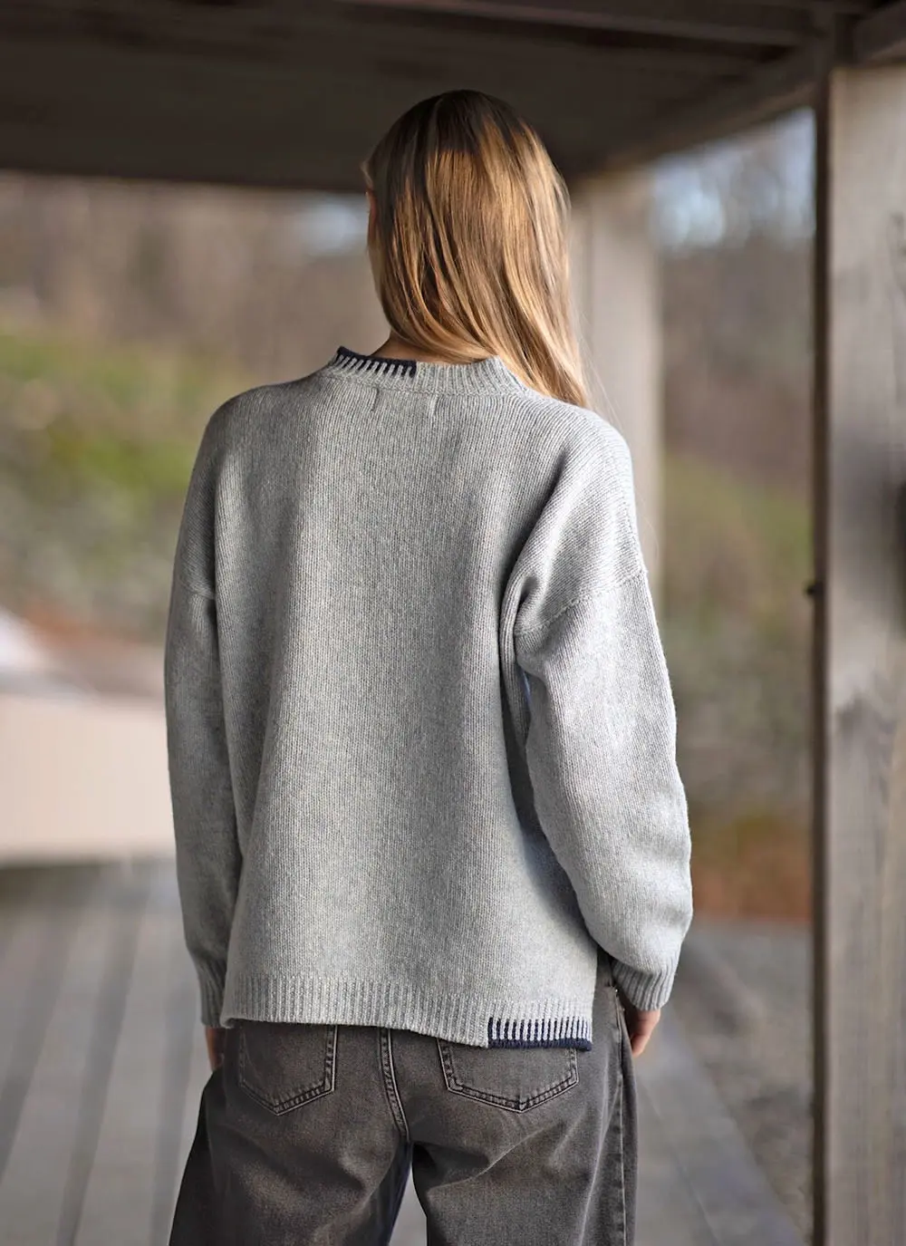 Blonde woman wearing grey woolen sweater with stables in background