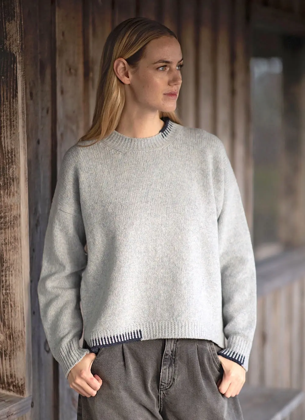 Blonde woman wearing grey woolen sweater with stables in background