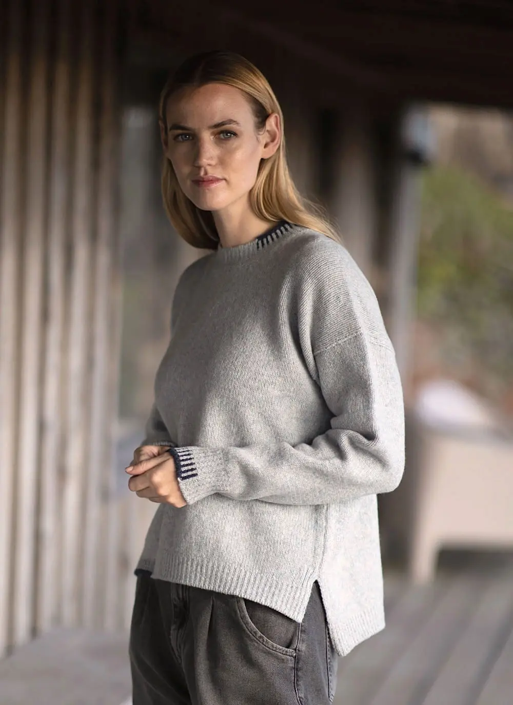 Blonde woman wearing grey woolen sweater with stables in background