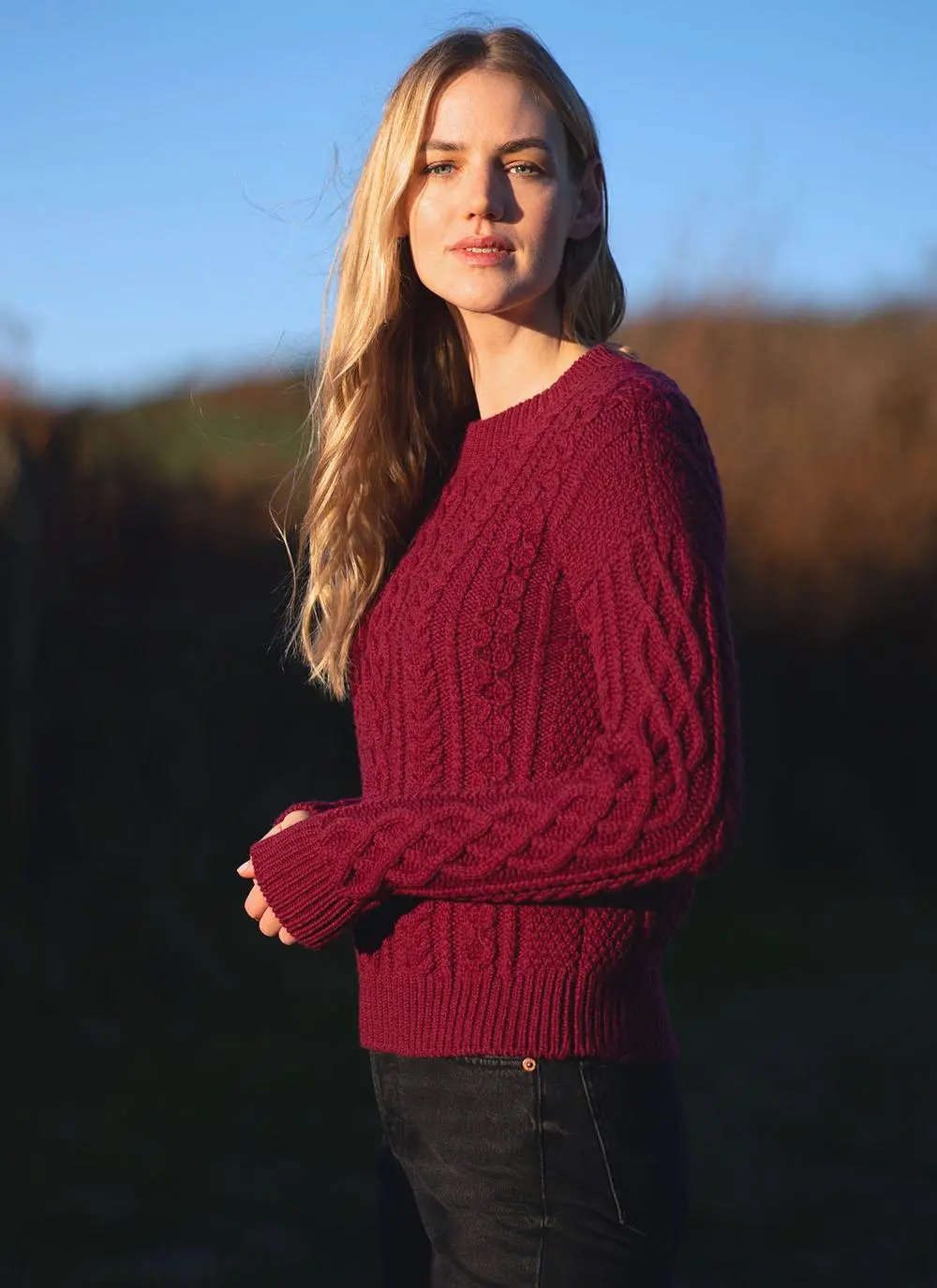 blonde woman wearing bright berry red sweater with aran stitch overall design