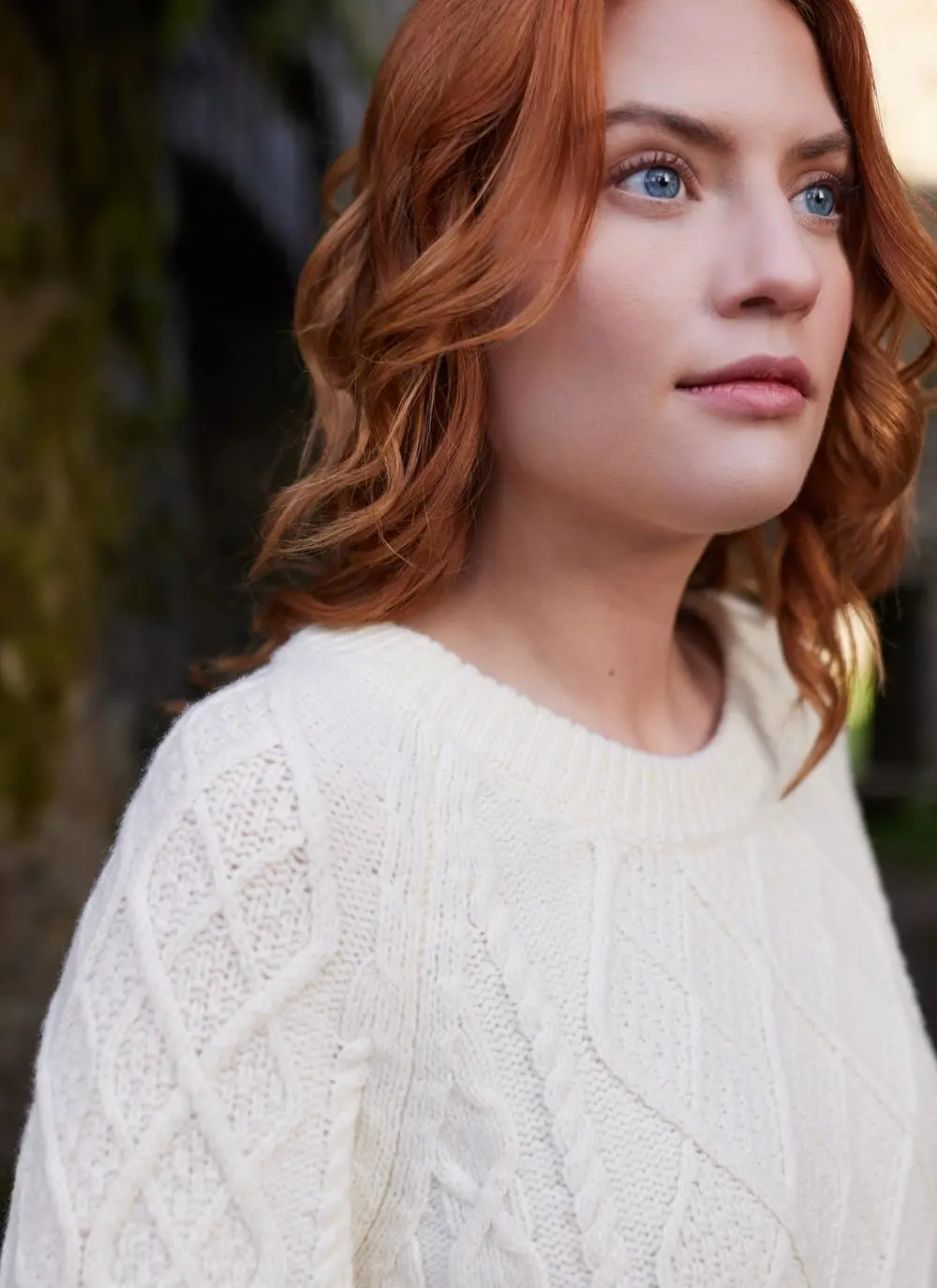 Close up shot of red haired woman in abbey wearing white Aran sweater 