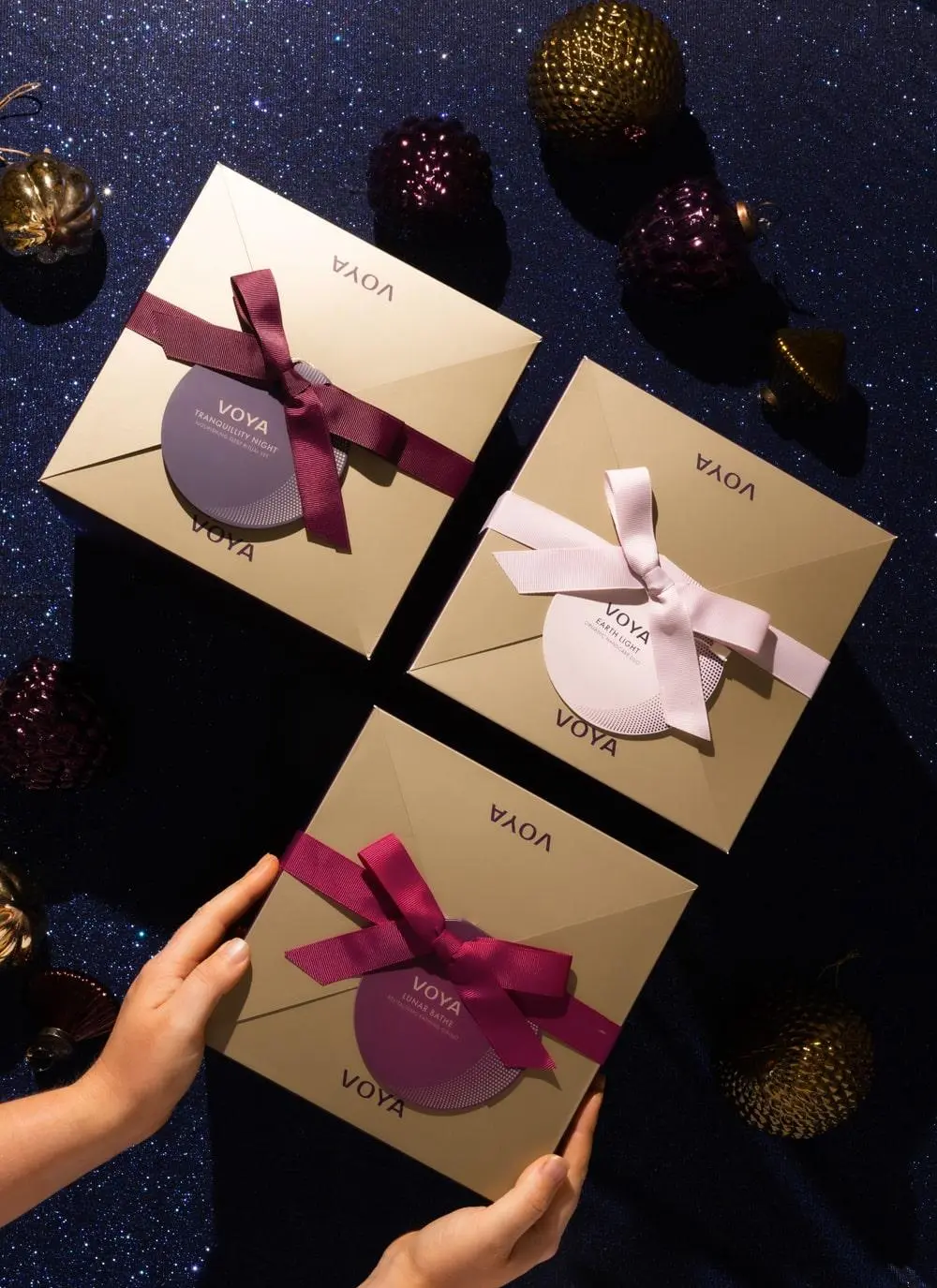 Voya Christmas Gift Set packaging trio against purple glittery festive background