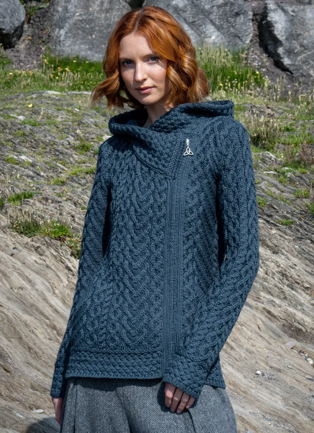 Red headed model standing in rocky area wearing a blue Aran biker hoodie