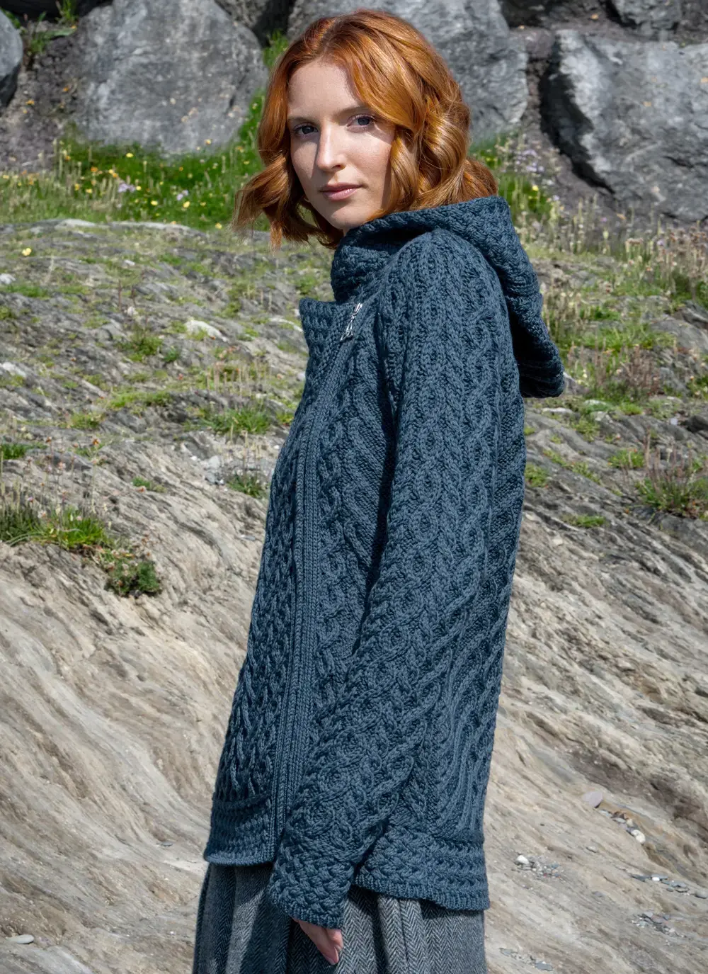 Red headed model in rocky area wearing a blue Aran biker hoodie standing to the side with hood down