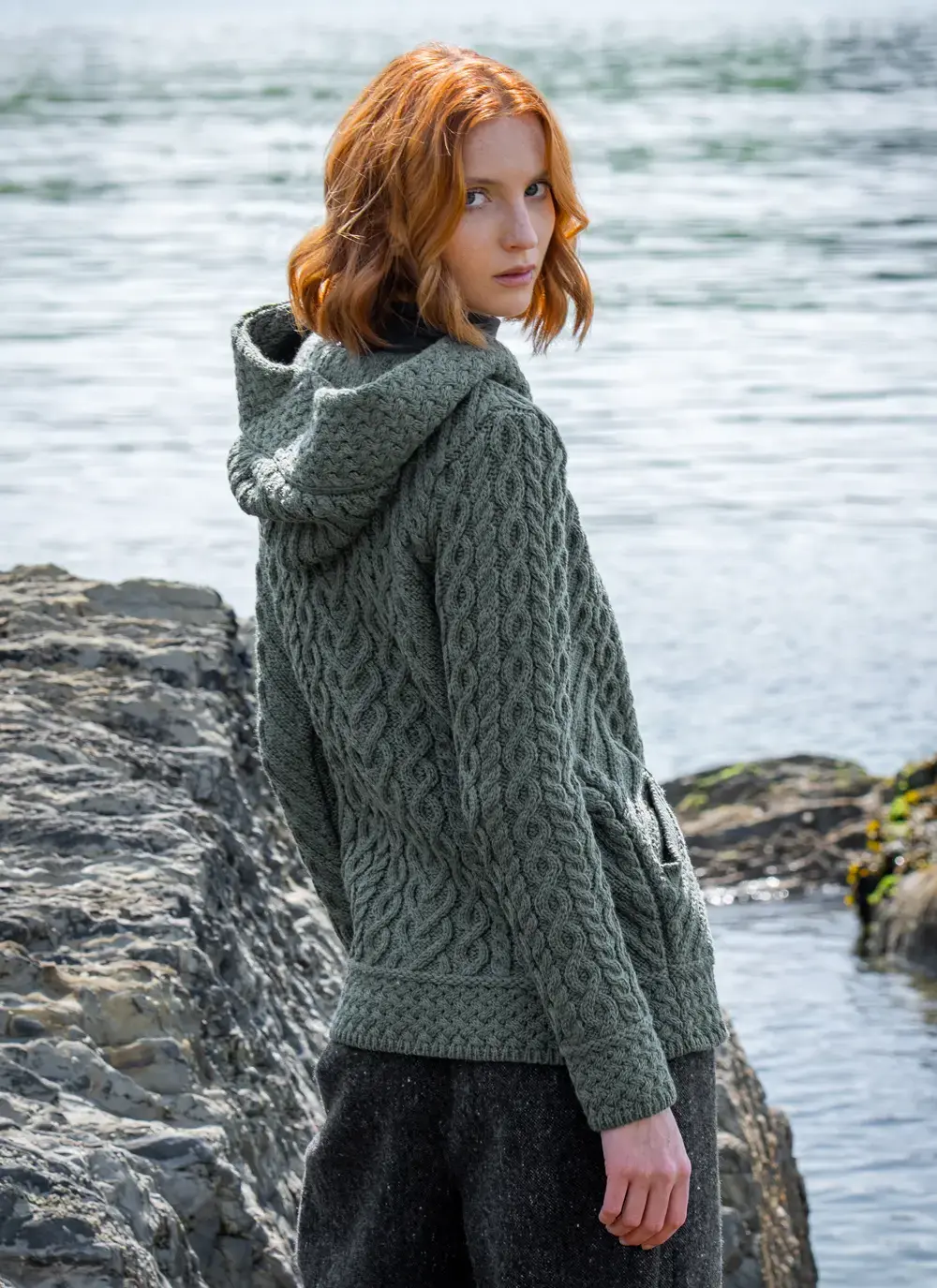 red head model at seaside in tundra aran cable knit biker hoodie looking over shoulder