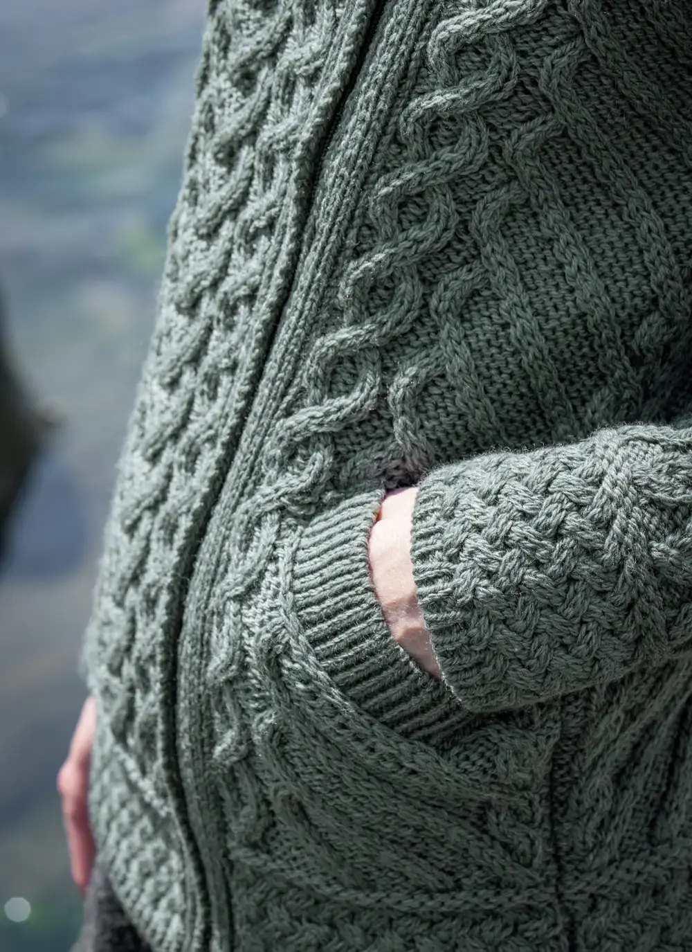Close up of red head model with sea background detail of pocket tundra aran cable knit biker hoodie