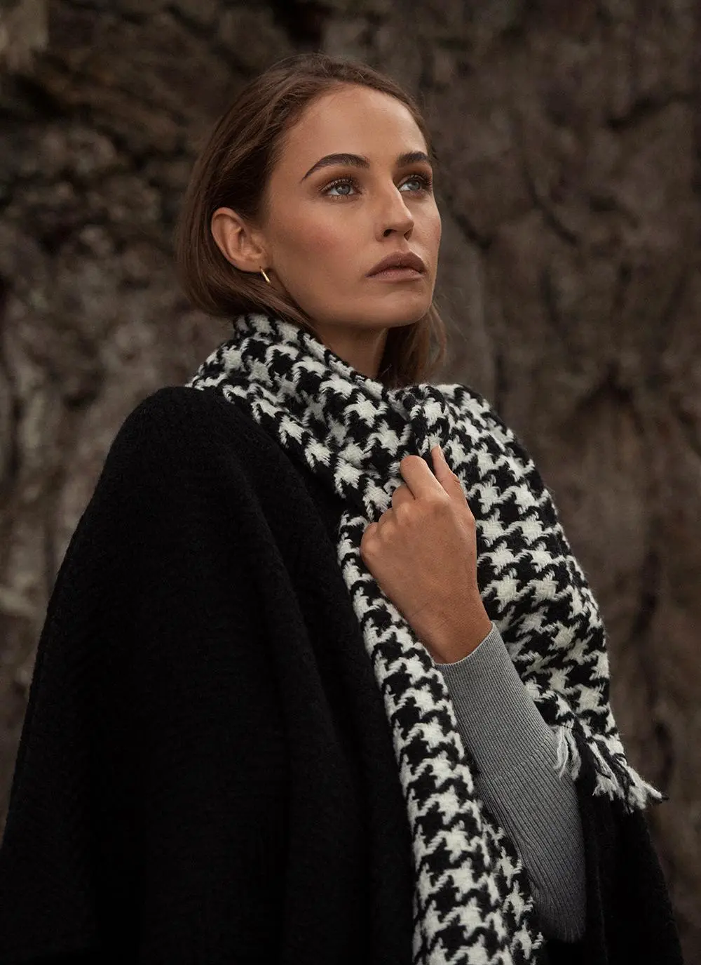 Close up shot of woman in woodland wearing black wool cape with houndstooth scarf.