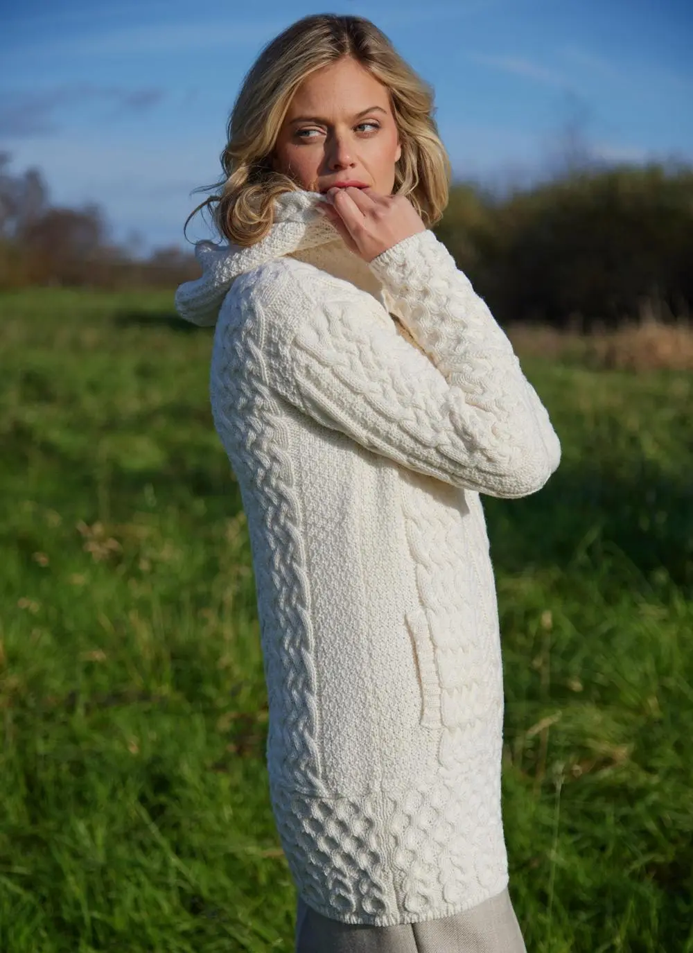 A blonde woman standing in field wearing celtic aran natural hoody