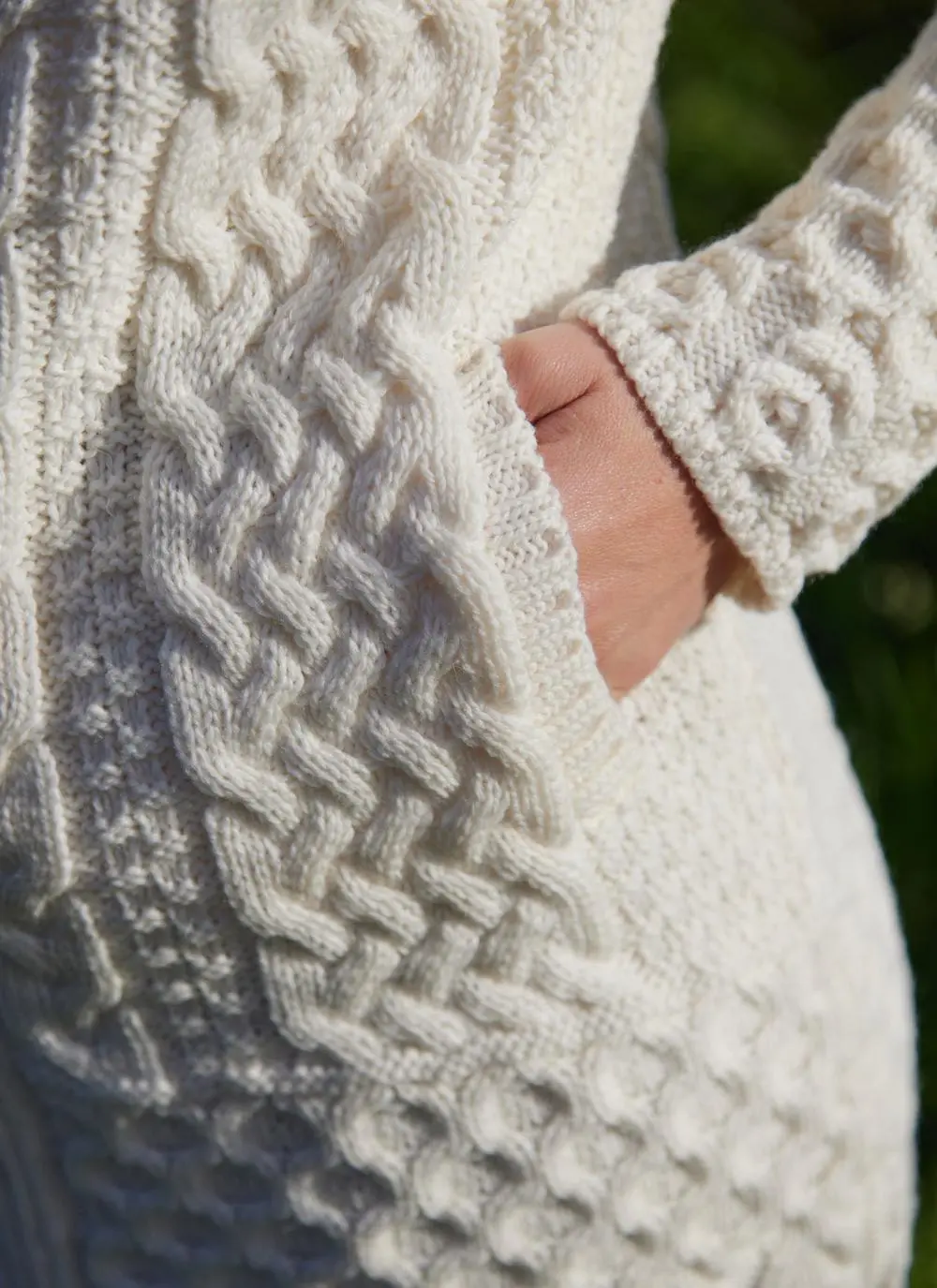 A blonde woman standing in field wearing celtic aran natural hoody, close up of pocket