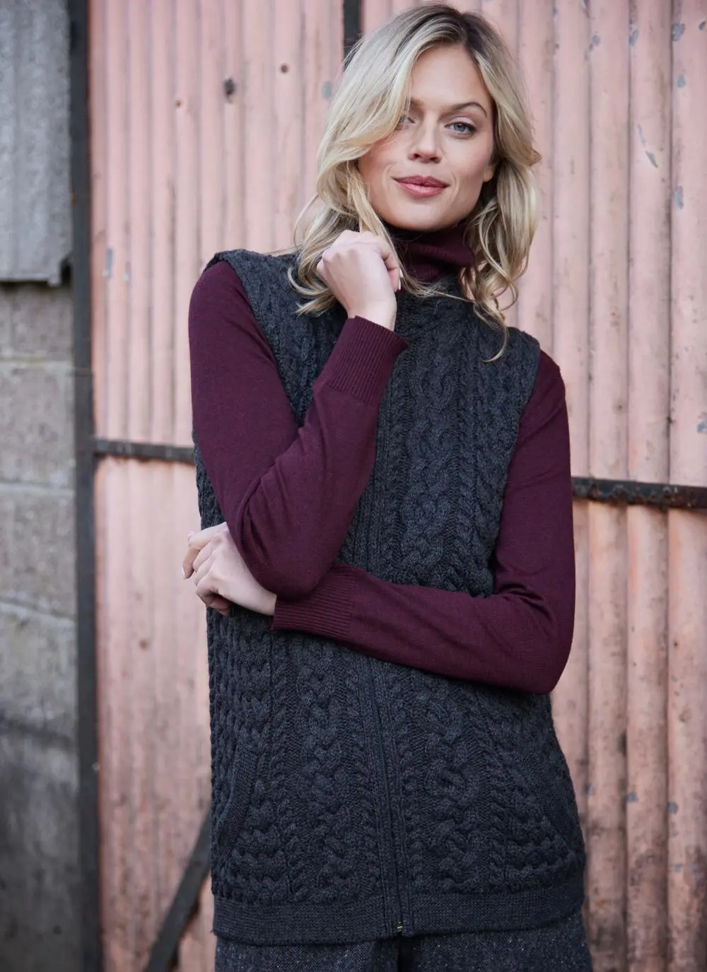 Women standing in front of pink door wearing charcoal aran gilet, posing