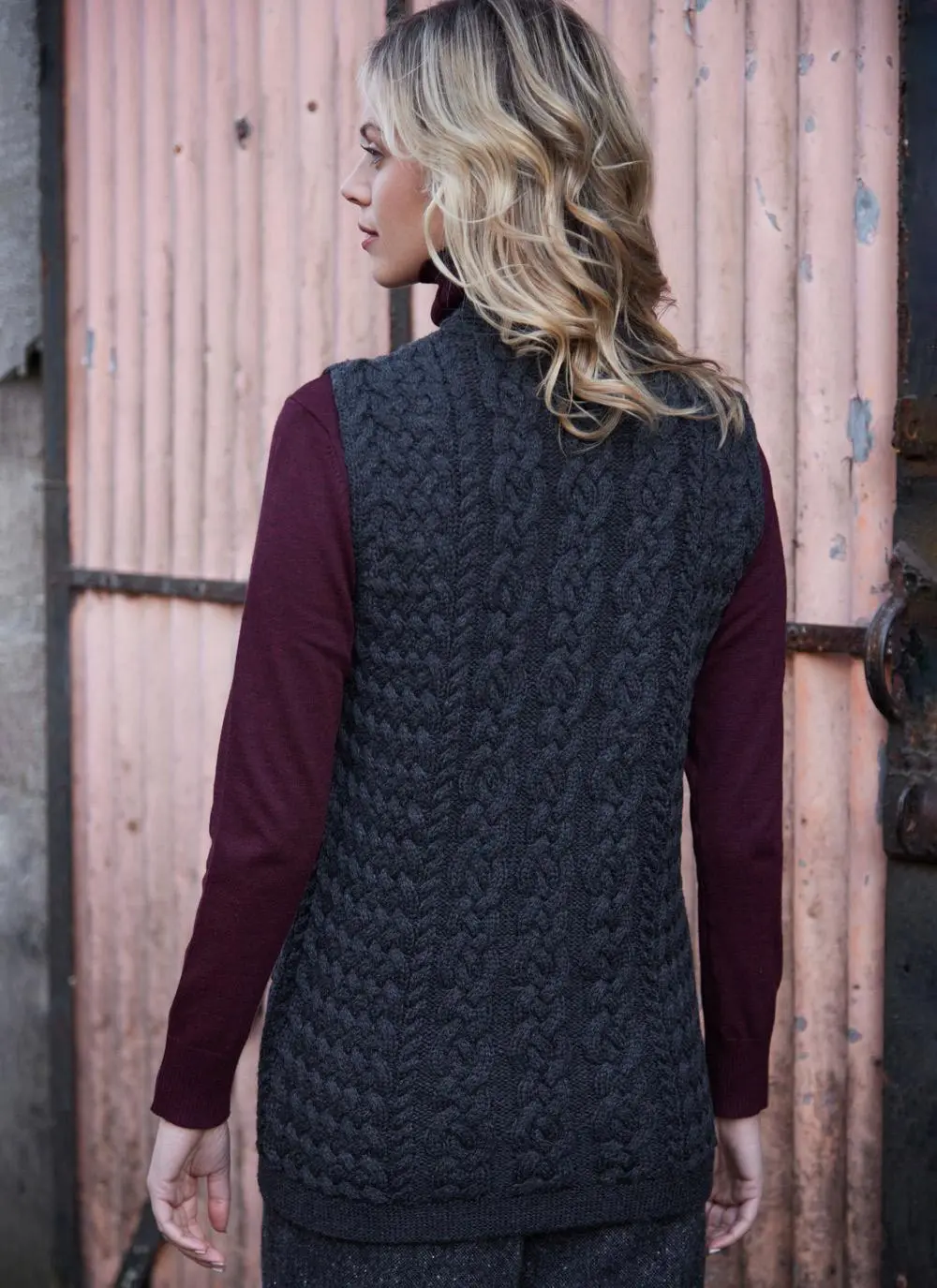 Women standing in front of pink door wearing charcoal aran gilet, back shot