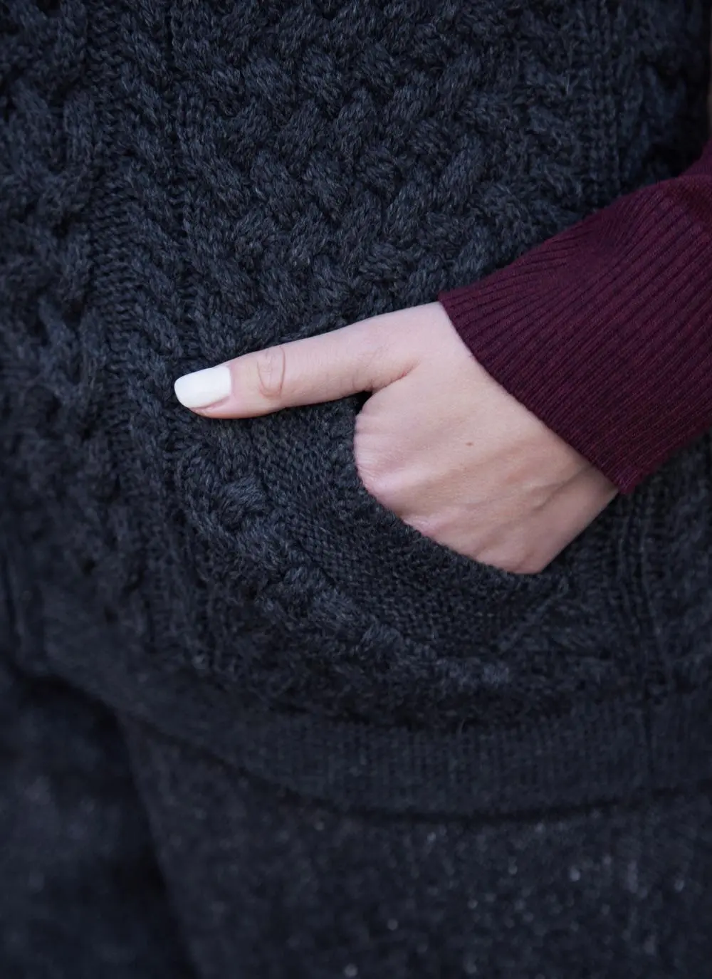 Women standing in front of pink door wearing charcoal aran gilet, close up of pocket