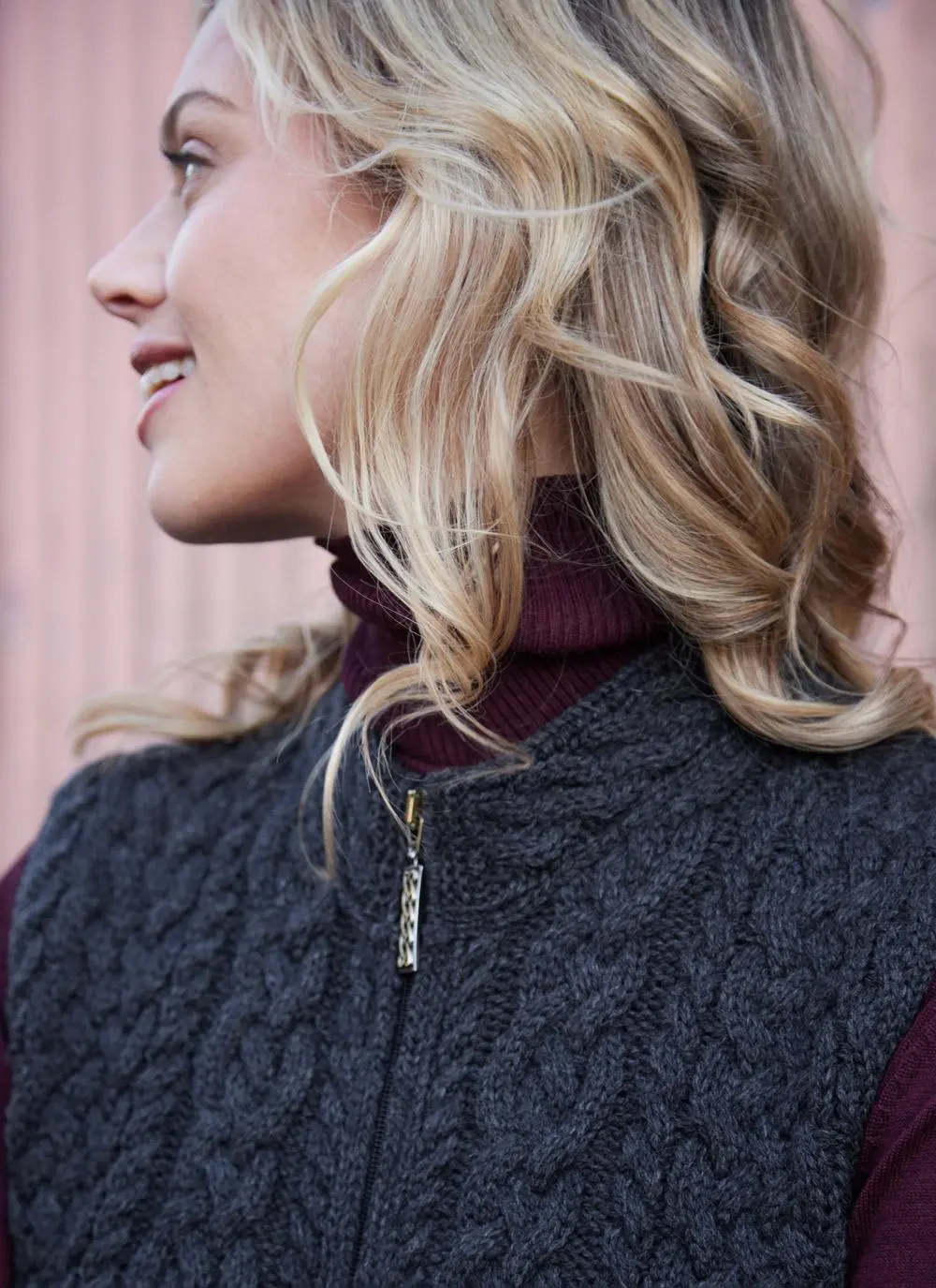 Women standing in front of pink door wearing charcoal aran gilet, close up