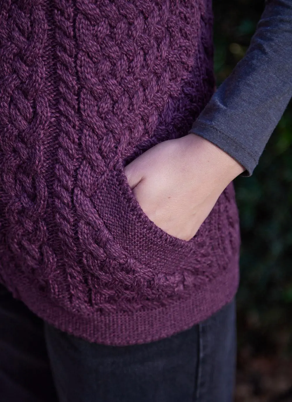 Women standing by trees wearing a purple aran gilet, pocket close up