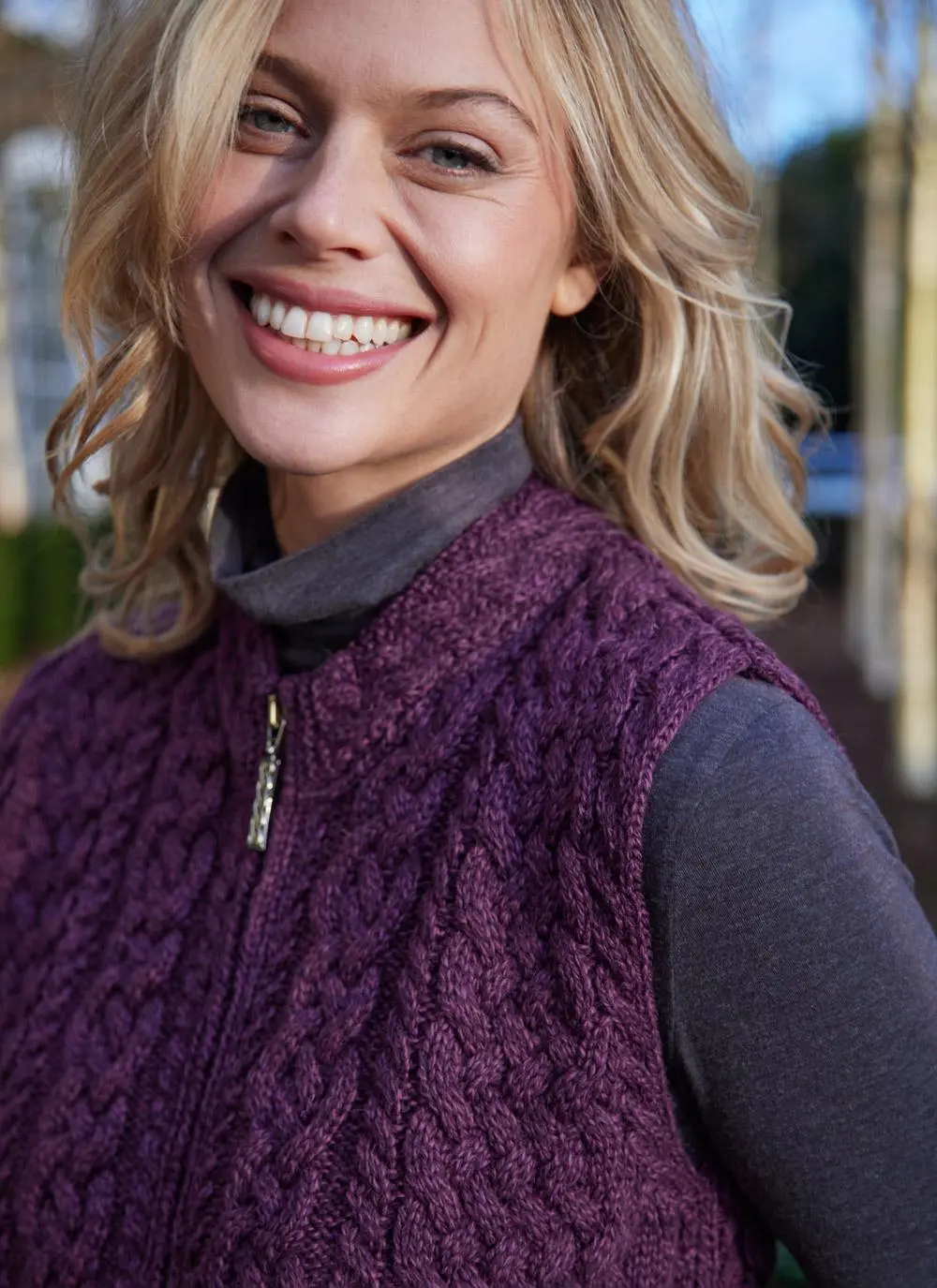 Women standing by trees wearing a purple aran gilet, close up