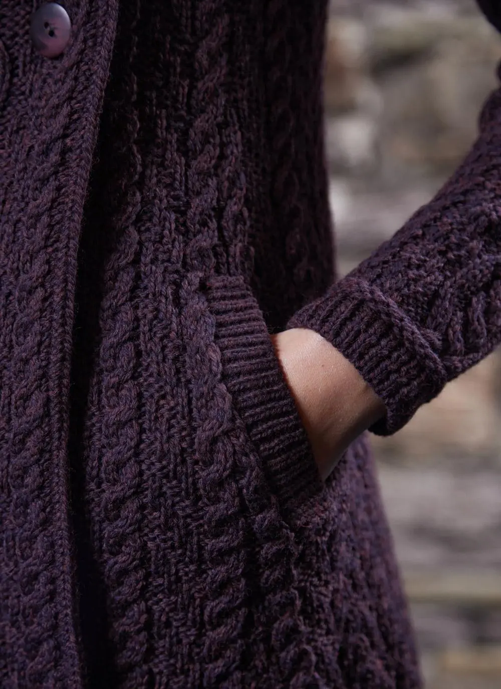 studio shot of blonde woman wearing dark purple aran long aran cardigan, close up of pocket