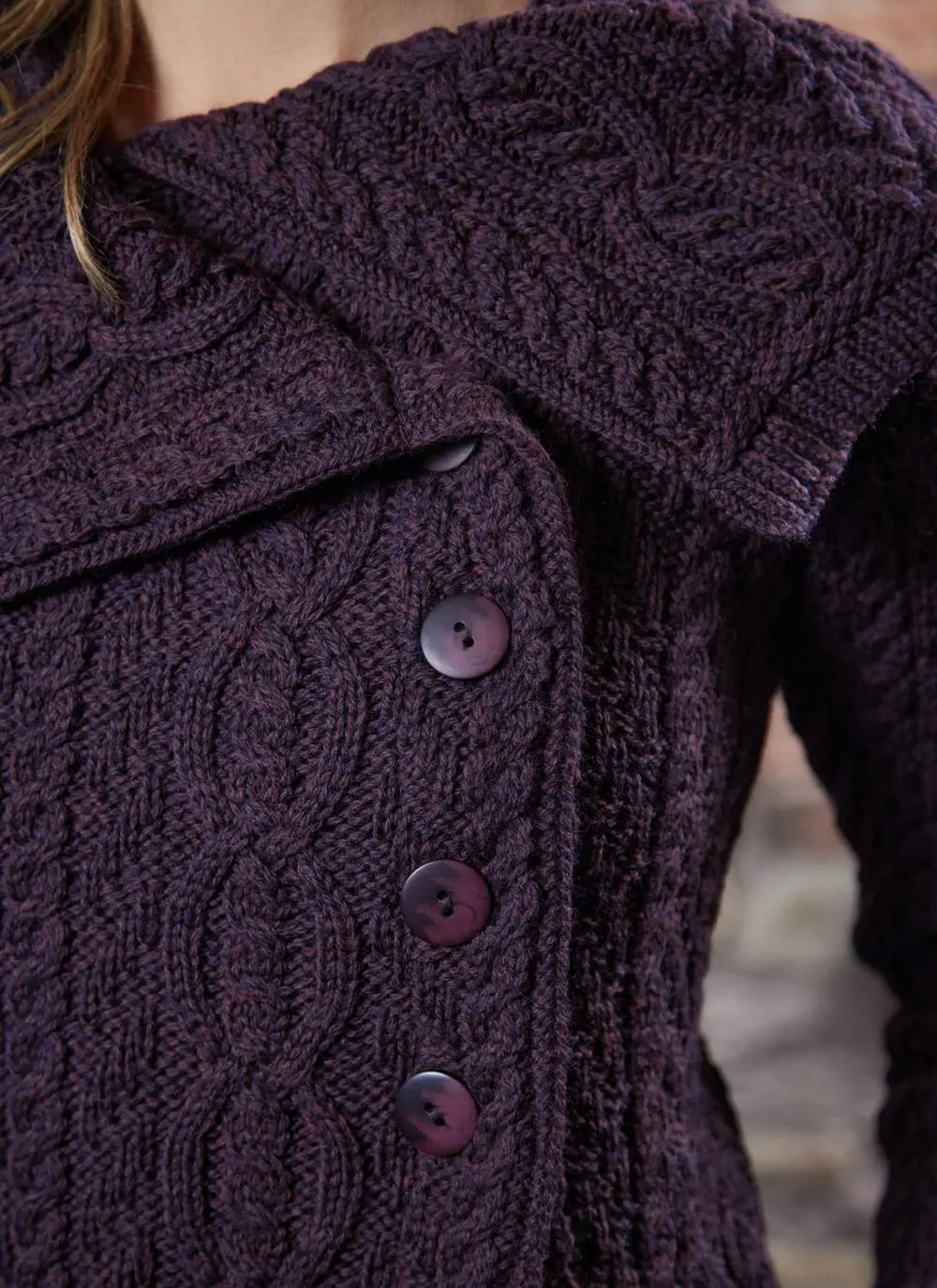 studio shot of blonde woman wearing dark purple aran long aran cardigan, close up of buttons