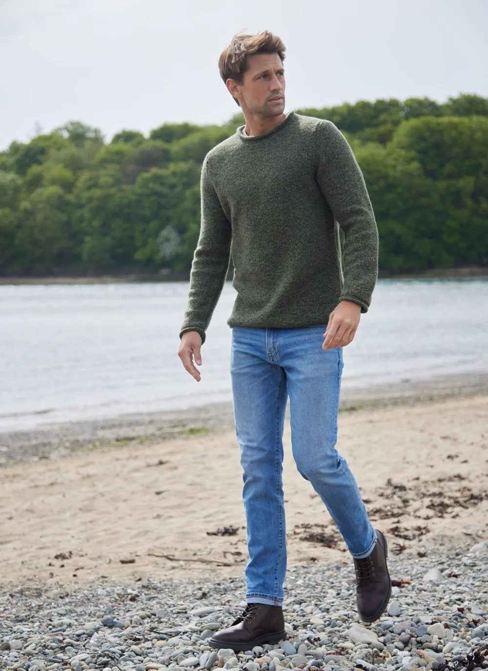 Man on beach wearing an olive green fisherman sweater with rolled neck and sleeves