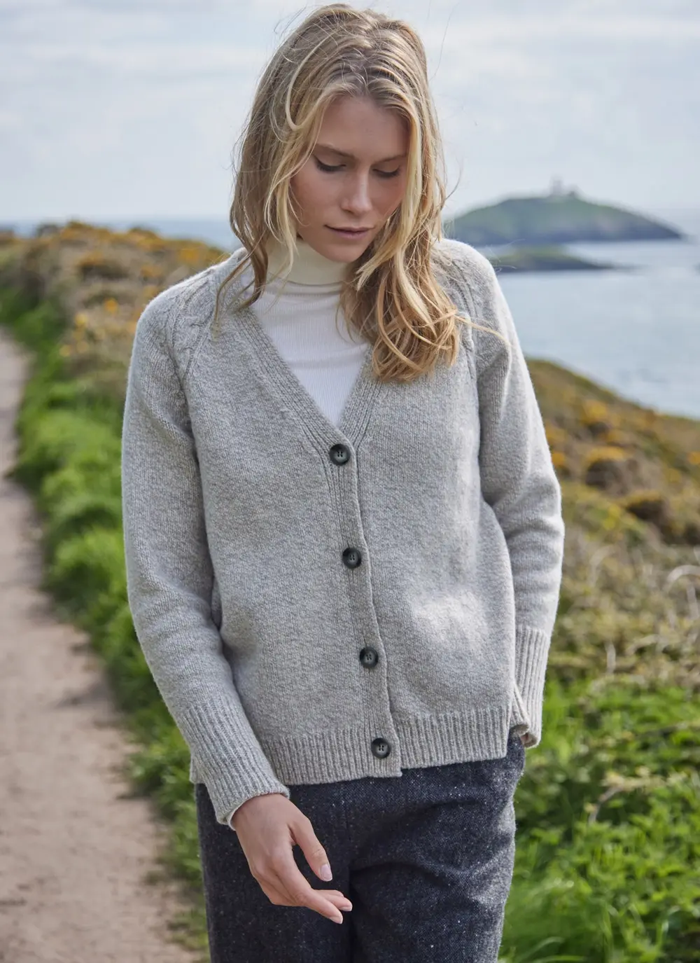Grey colored knit cardigan, ribbed cuffs and hem, with model on a cliff walk
