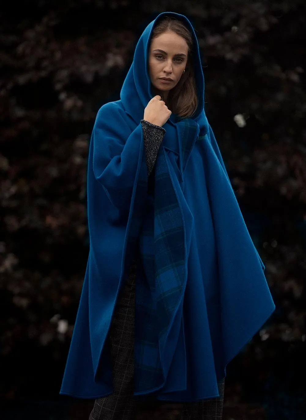 Woman standing outside wearing blue cape with hood.