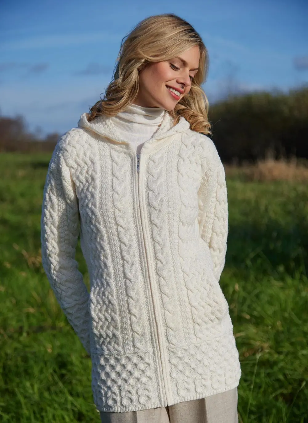 A blonde woman standing in field wearing celtic aran natural hoody