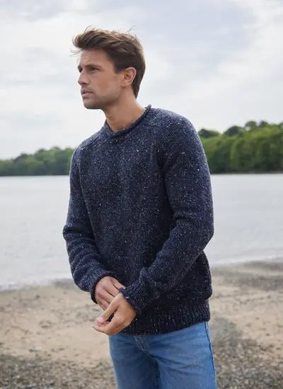 brown haired man standing on beach wearing navy sweater clasping hands