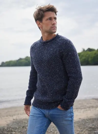 brown haired man walking along on beach wearing navy sweater