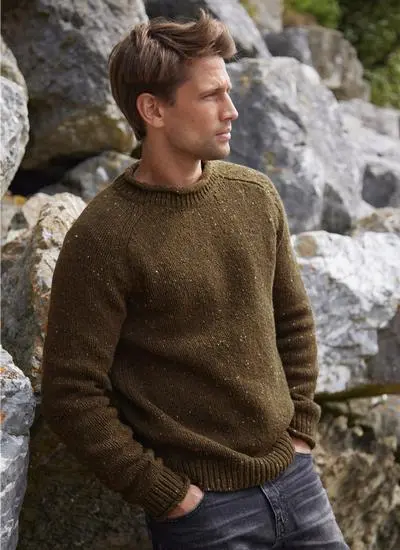 man leaning on rocks wearing olive colored knit sweater, hands in pockets