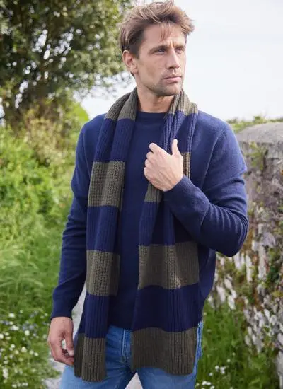man standing on grassy path wearing blue and green striped knit scarf