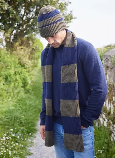 man standing on grassy path wearing blue and green striped knit scarf and matching hat