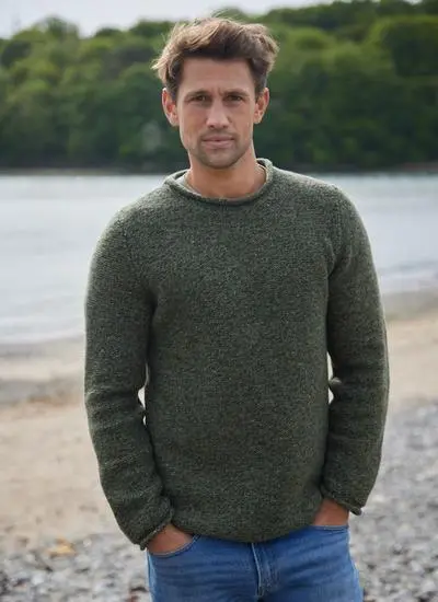 Man on beach wearing an olive green fisherman sweater with rolled neck and sleeves