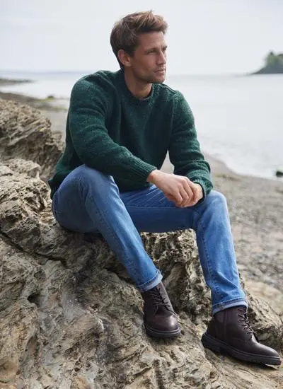 Man sitting on a rock on a beach in a bottle green fisherman flecked crew neck sweater