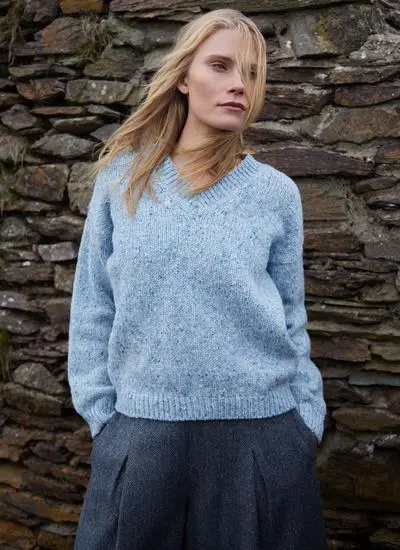 blonde woman standing against stone wall wearing light blue knit sweater