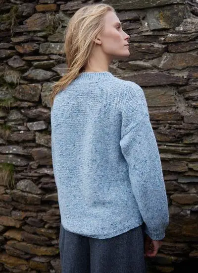 back shot of a blonde woman standing near stone wall wearing light blue knit sweater