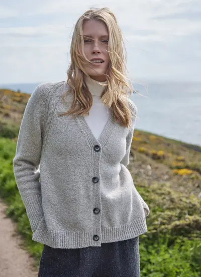 Grey colored knit cardigan, ribbed cuffs and hem, with model on a cliff walk