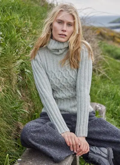 woman sitting in grass wearing a neutral colored turtle neck aran sweater
