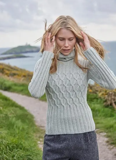 woman with wind in her hair wearing a neutral colored turtle neck aran sweater