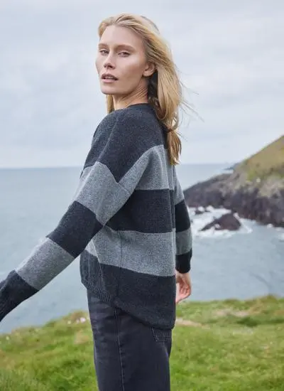 side angle of blonde woman standing by Irish cliffs on a windy day wearing a grey stripe sweater
