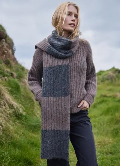 blonde woman standing in grassy coastal area wearing a copper and grey knit scarf