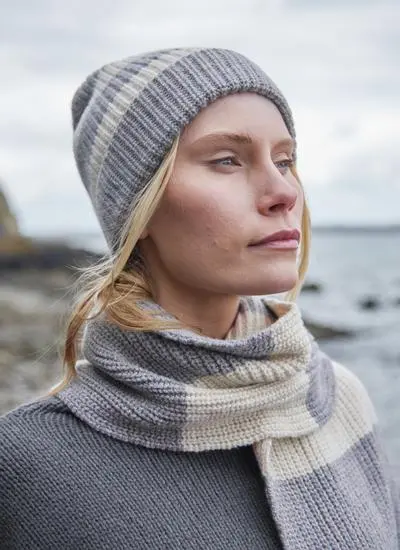 blonde woman wearing grey and white striped hat with a grey sweater and coastal background