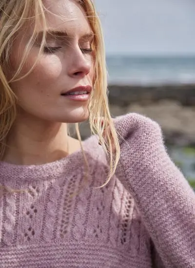 close up shot of blonde woman standing in rocky beach wearing a pink eyelet crew knit sweater