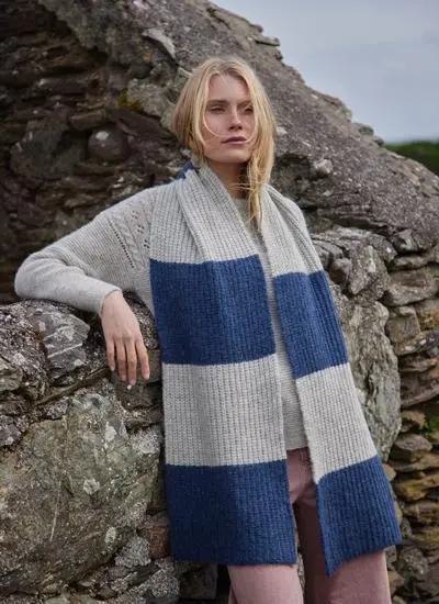 blonde woman leaning against rock wearing a large grey and blue knit scarf 