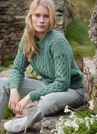 blonde woman sitting in grassy area wearing sage aran sweater