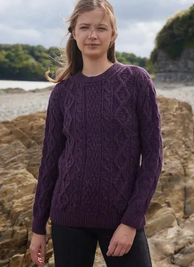 woman standing in rocky beach wearing purple aran sweater