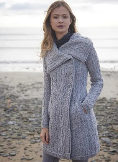 brunette woman standing on beach on cloudy morning wearing long grey aran cardigan with one hand in pocket