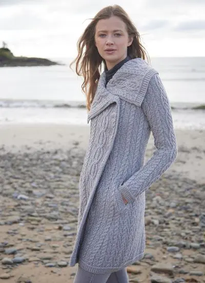 brunette woman standing on beach on cloudy morning wearing long grey aran cardigan with one hand in pocket